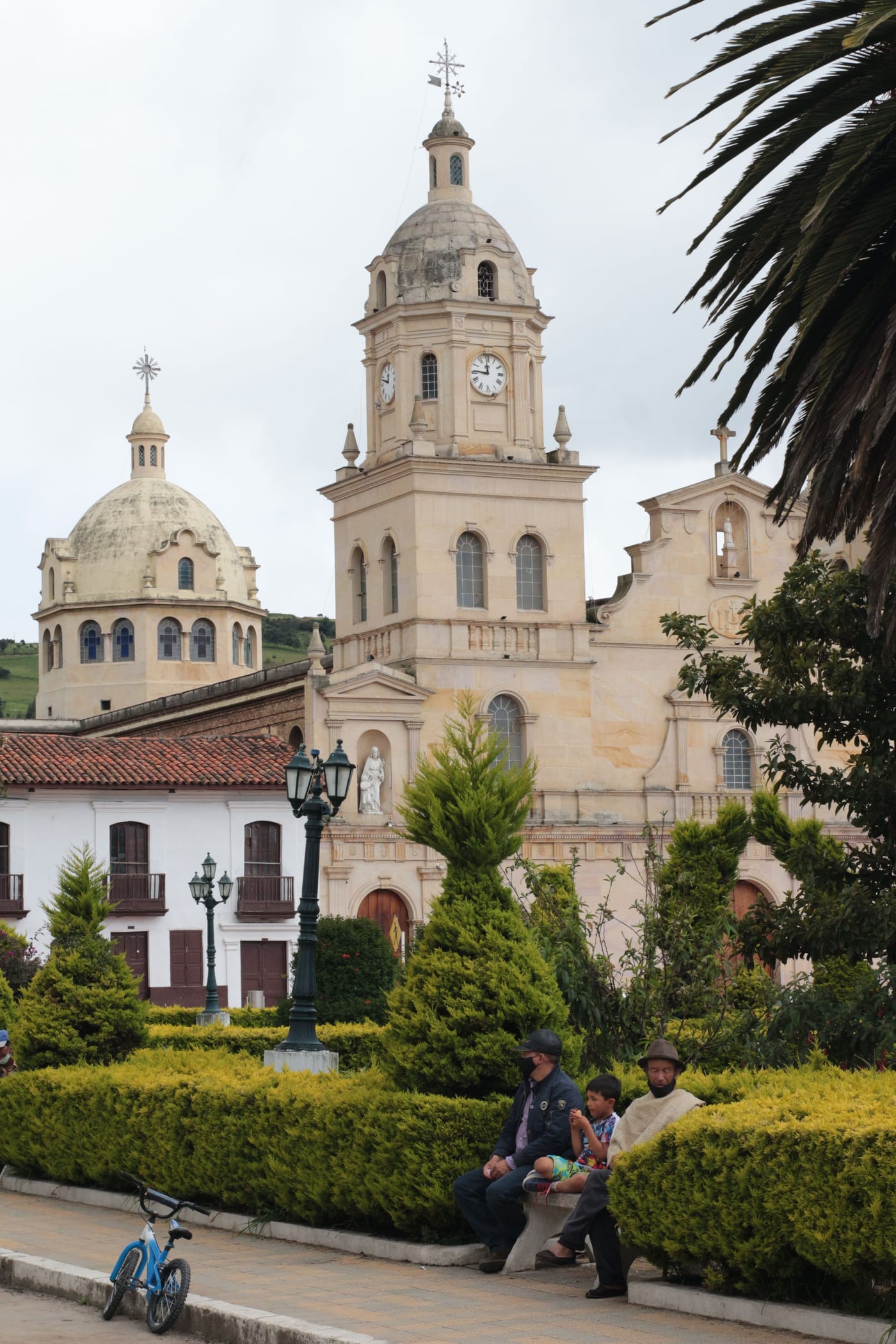 Torres de la catedral con reloj en la plaza principal, con visitantes descansando en las bancas