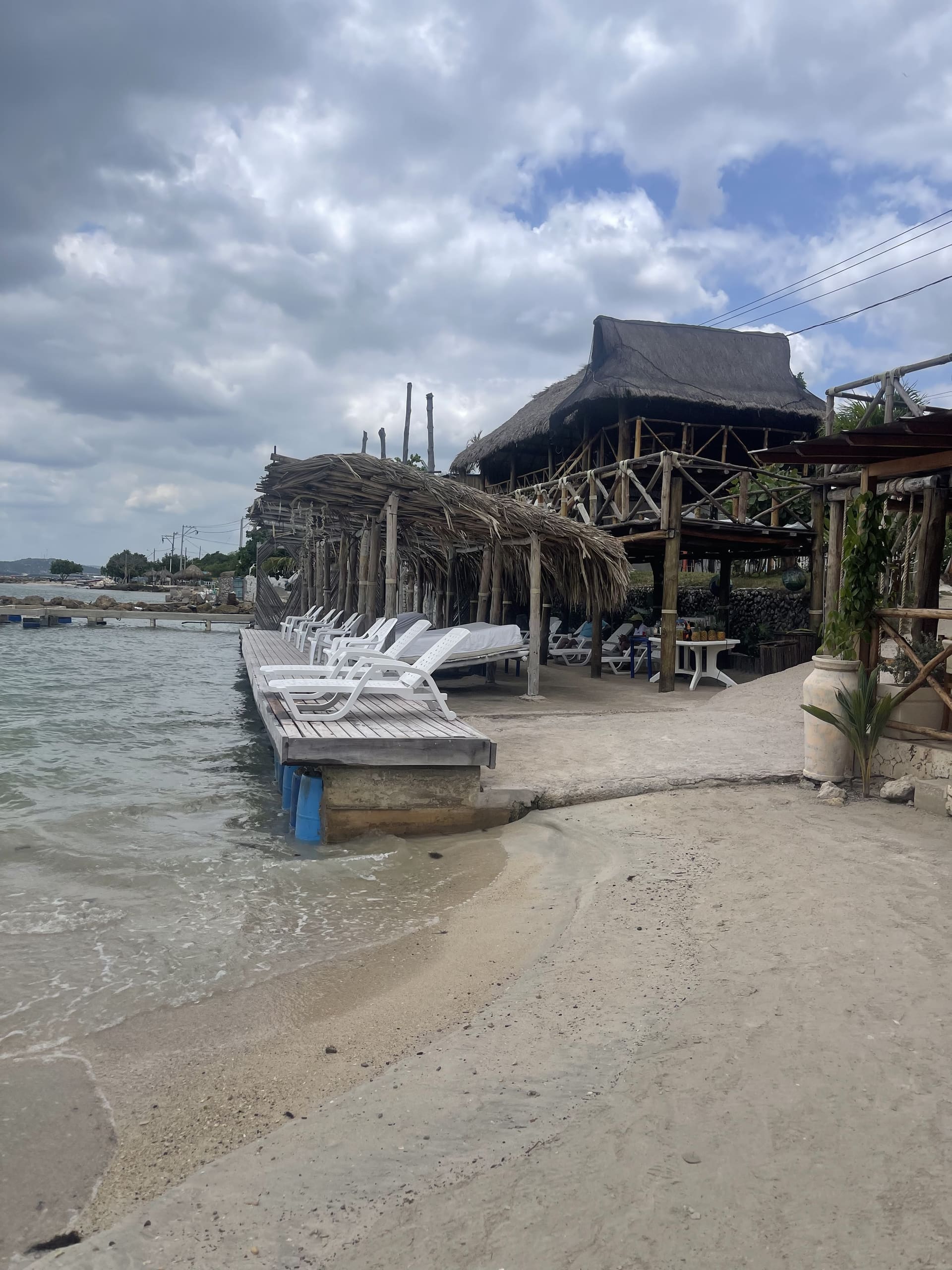 Club de playa con muelle de madera, camas solares y palapa de palma en la costa de Cartagena