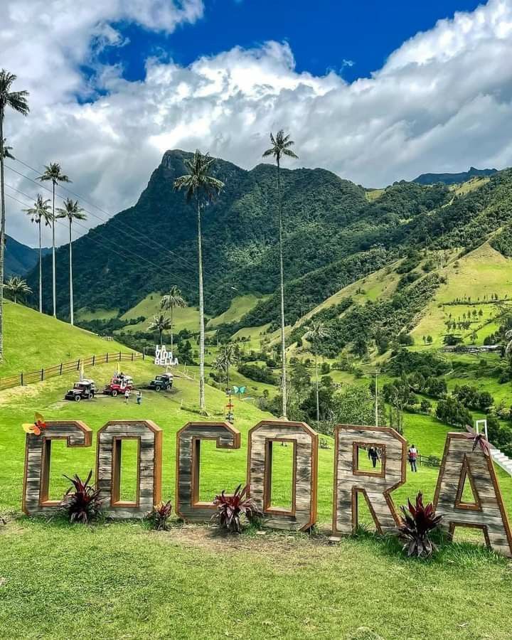 Letras gigantes de COCORA en el Valle de Cócora rodeadas de palmas de cera, con turistas paseando en cuatrimoto