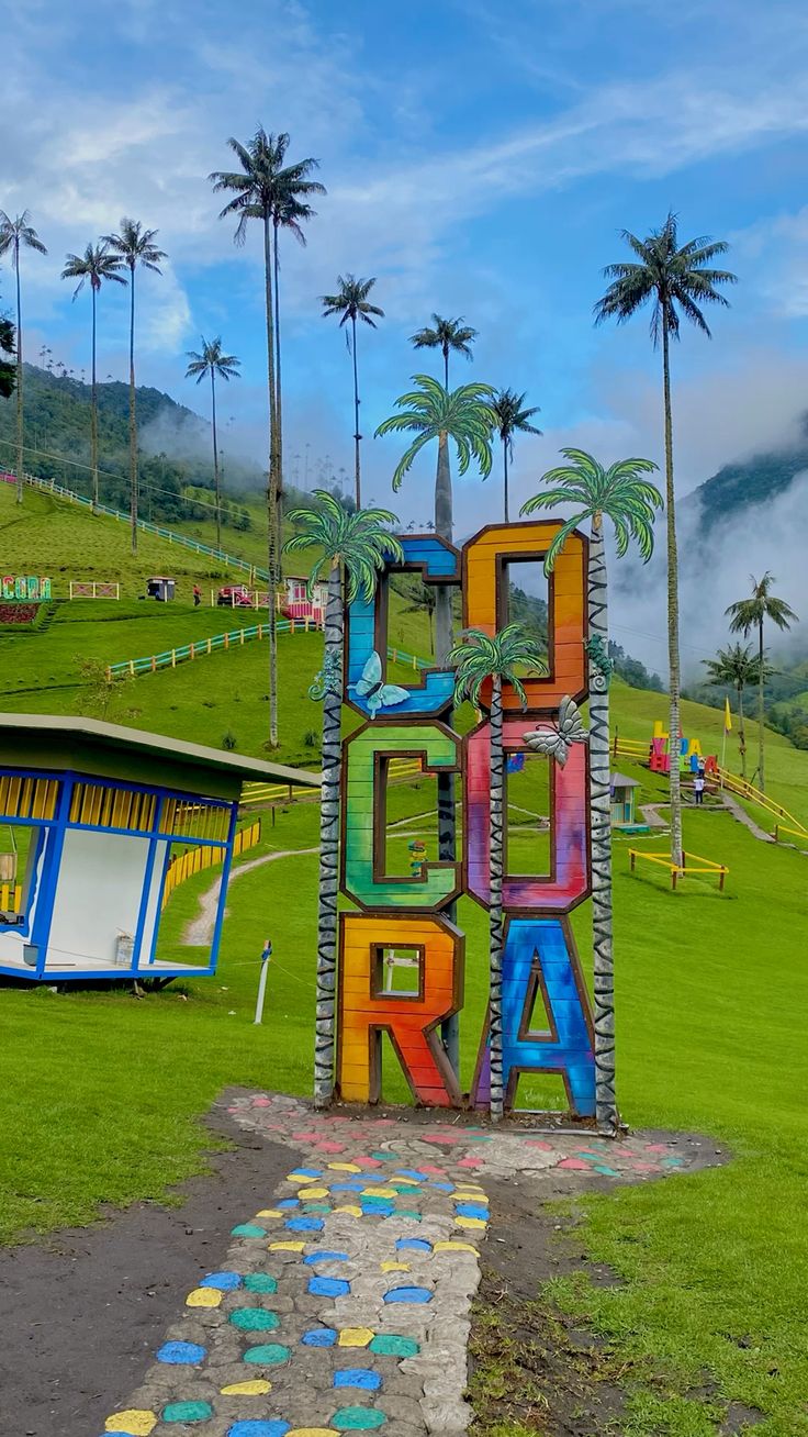 Letras coloridas de Cócora en un prado verde junto a un pequeño kiosco, con palmas de cera al fondo