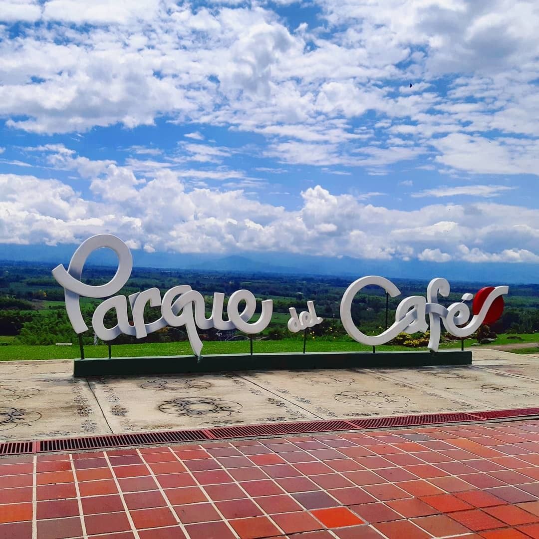 Letrero de entrada al Parque del Café sobre una plaza de baldosas rojas