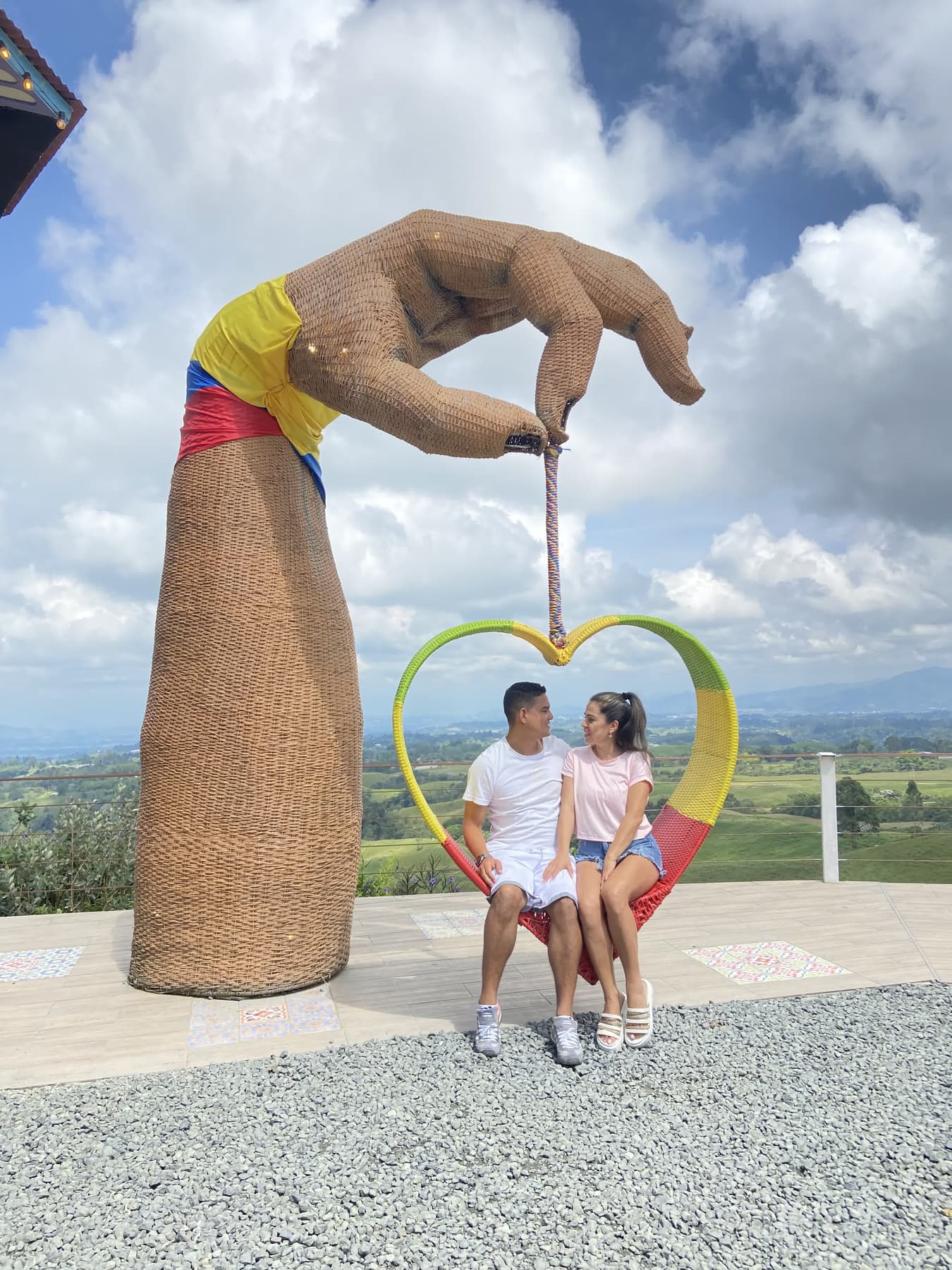 Pareja posando junto a una escultura de una mano con un corazón y la bandera de Colombia en el Eje Cafetero