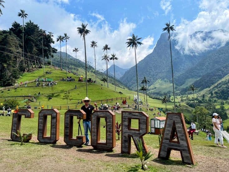 Turista junto a las letras blancas de Cócora con palmas de cera de fondo en el Valle de Cócora