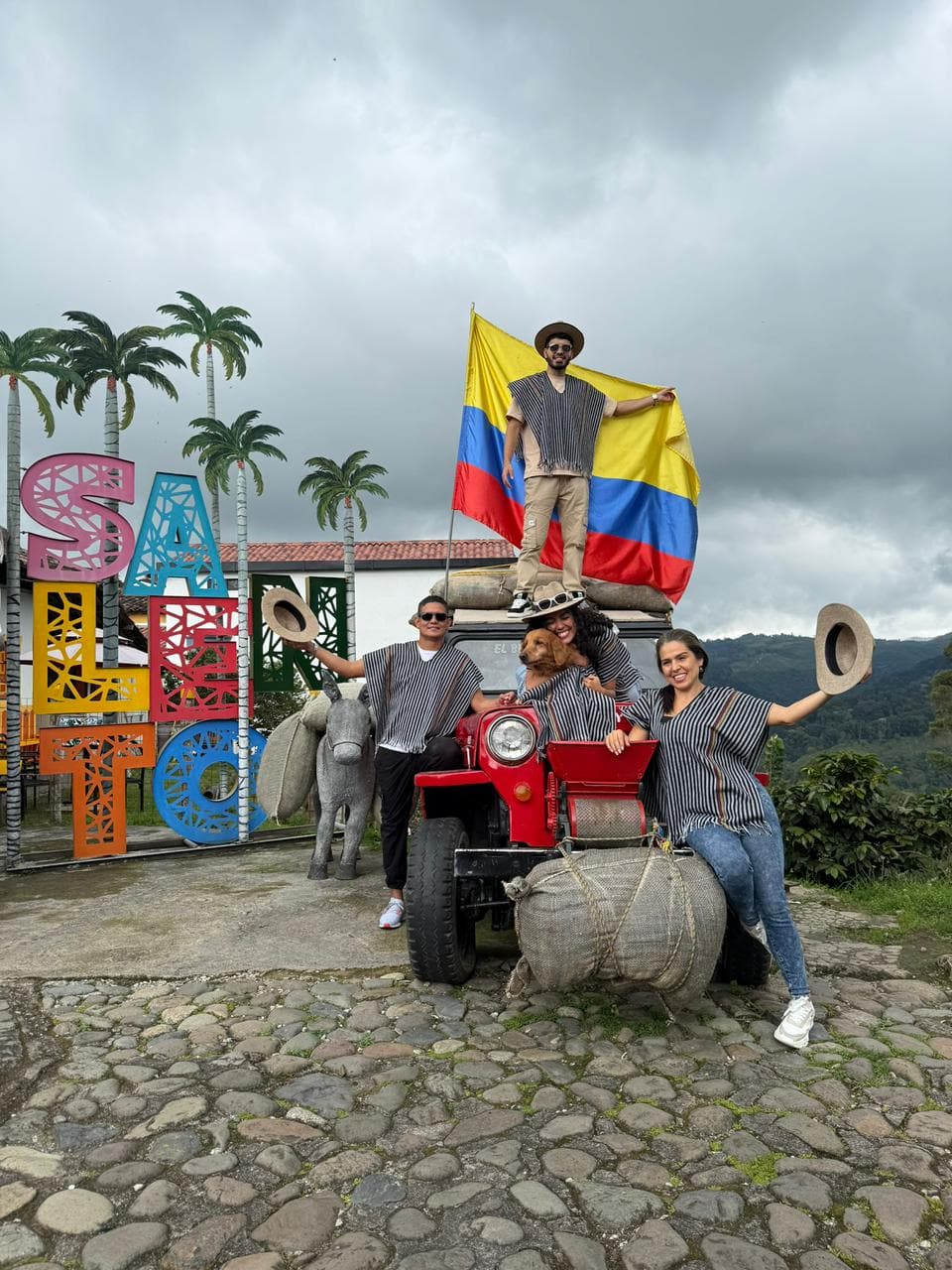 Familia posando en un Jeep Willys con la bandera de Colombia frente a un mural colorido de Salento
