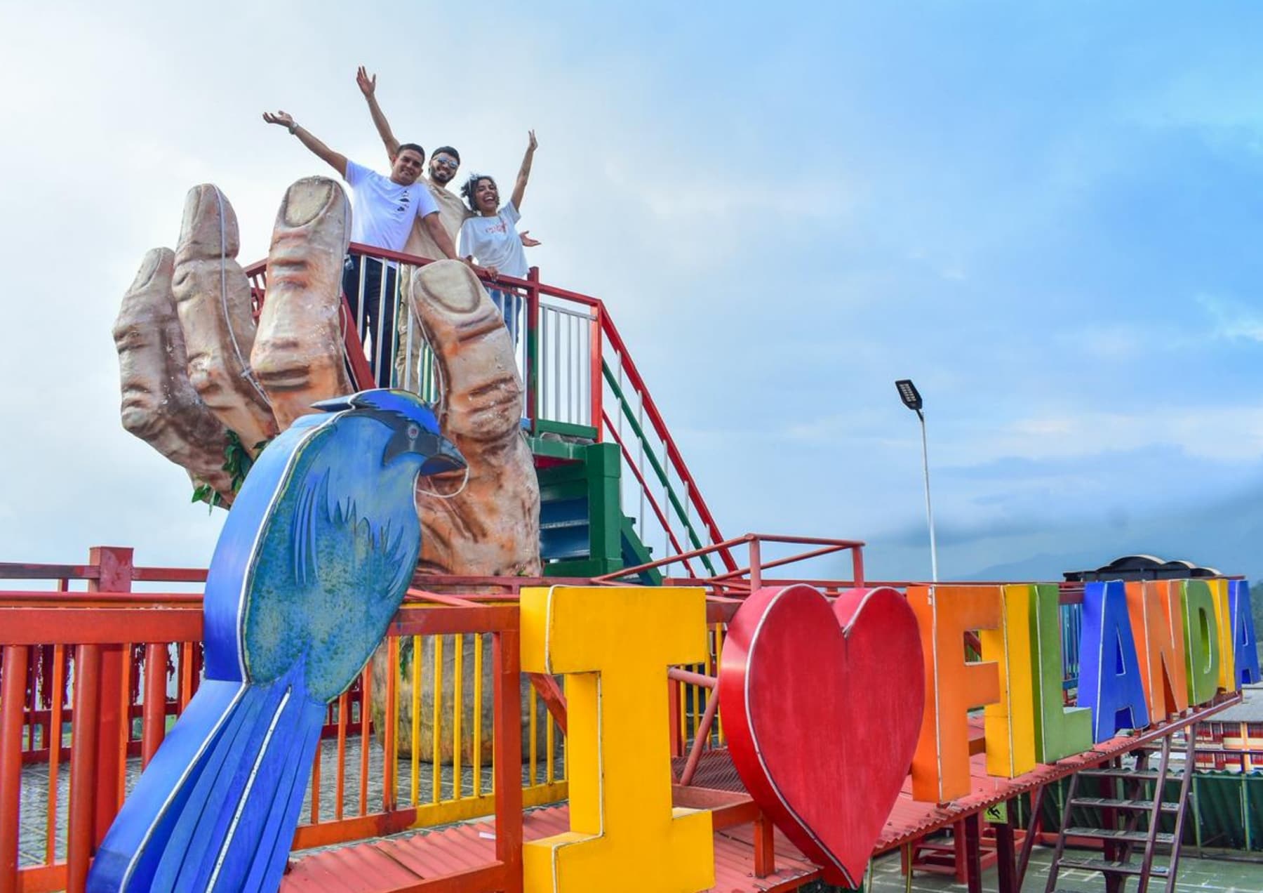 Turistas saludando desde un mirador colorido en Filandia, decorado con una escultura de guacamaya