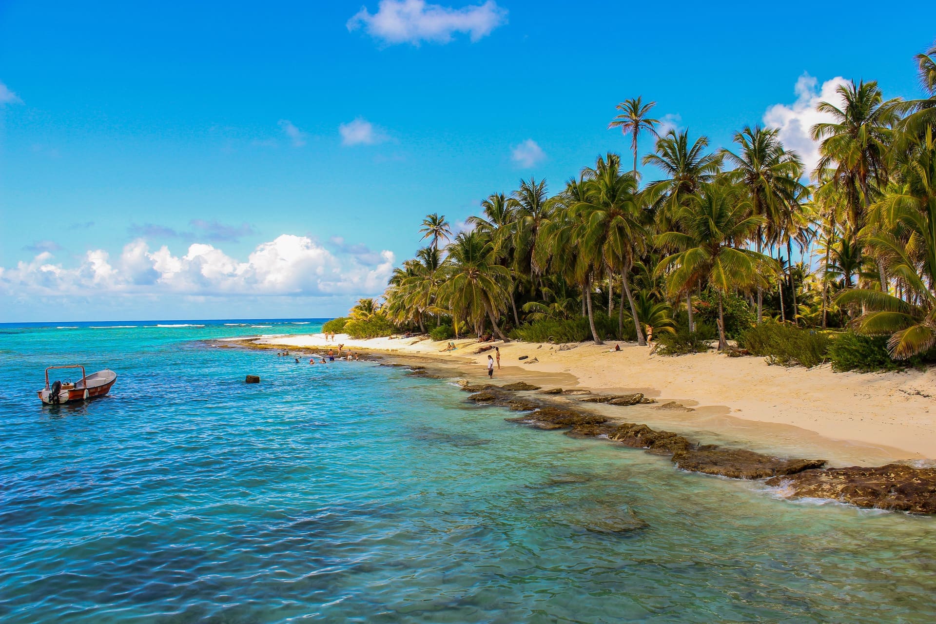 Playa de arena blanca con palmeras y una lancha anclada en el mar de siete colores de San Andrés