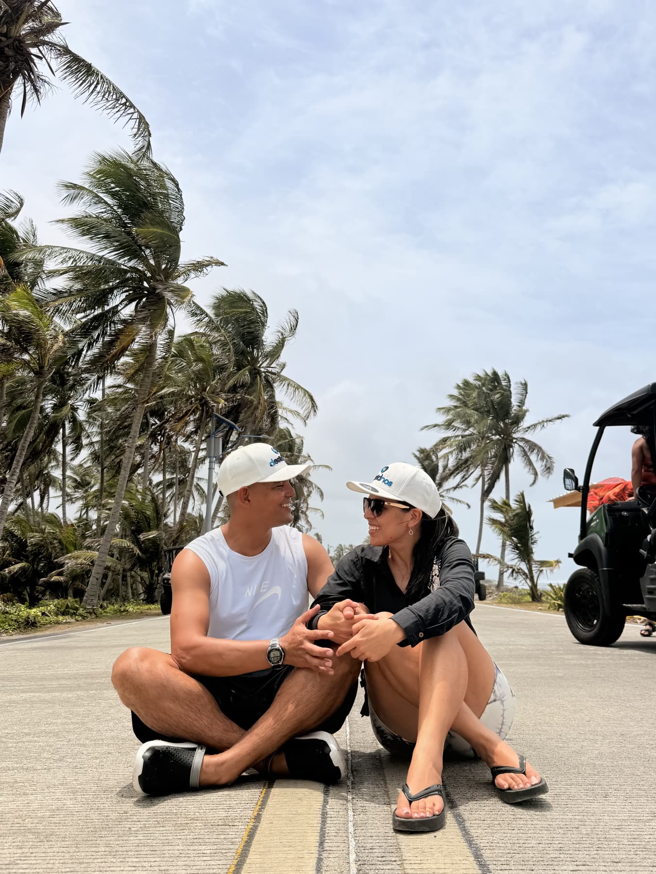 Pareja de turistas descansando junto a los carritos de golf en una vía bordeada de palmeras