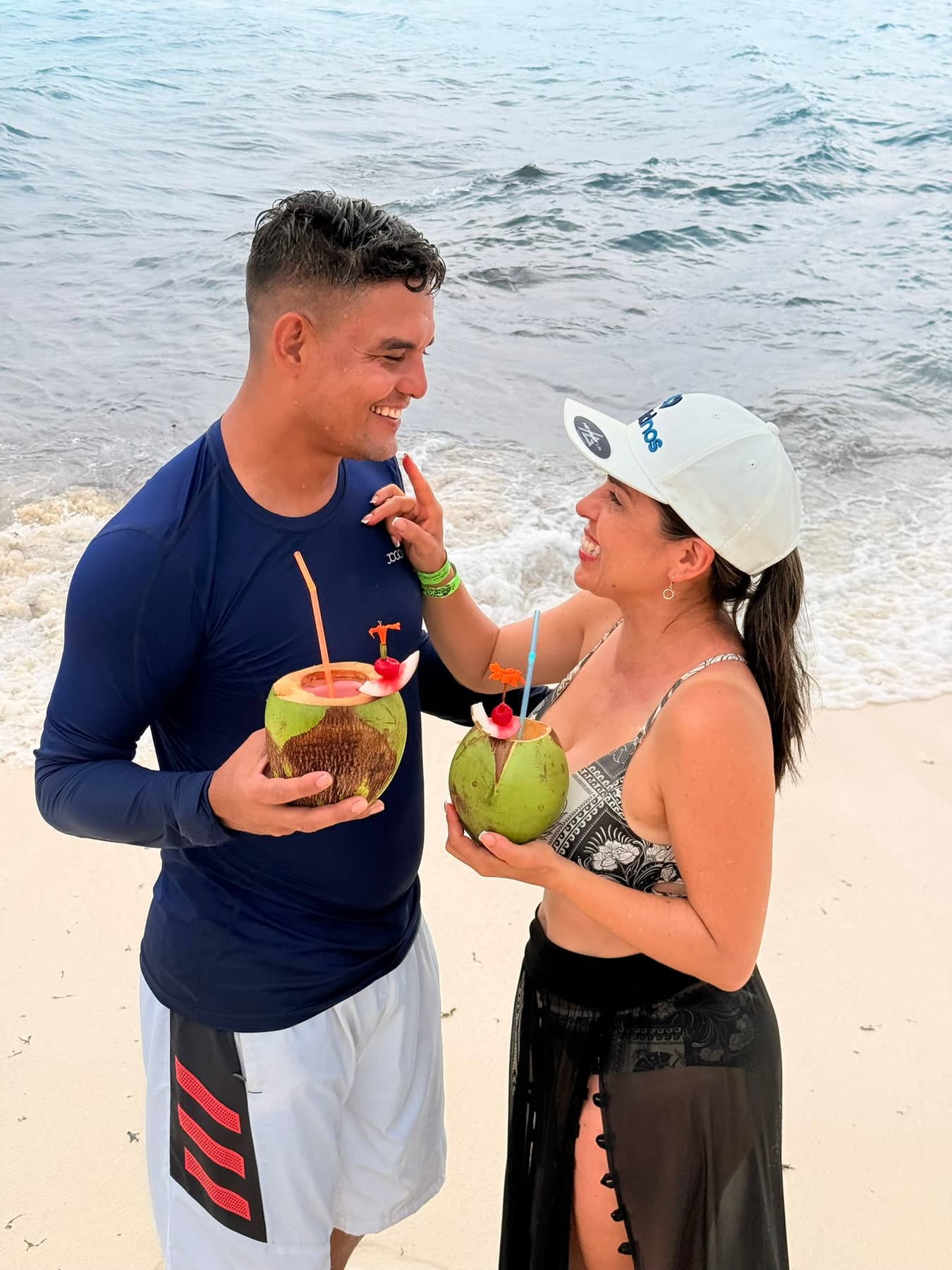 Pareja de turistas sonriendo mientras beben agua de coco en la playa de San Andrés