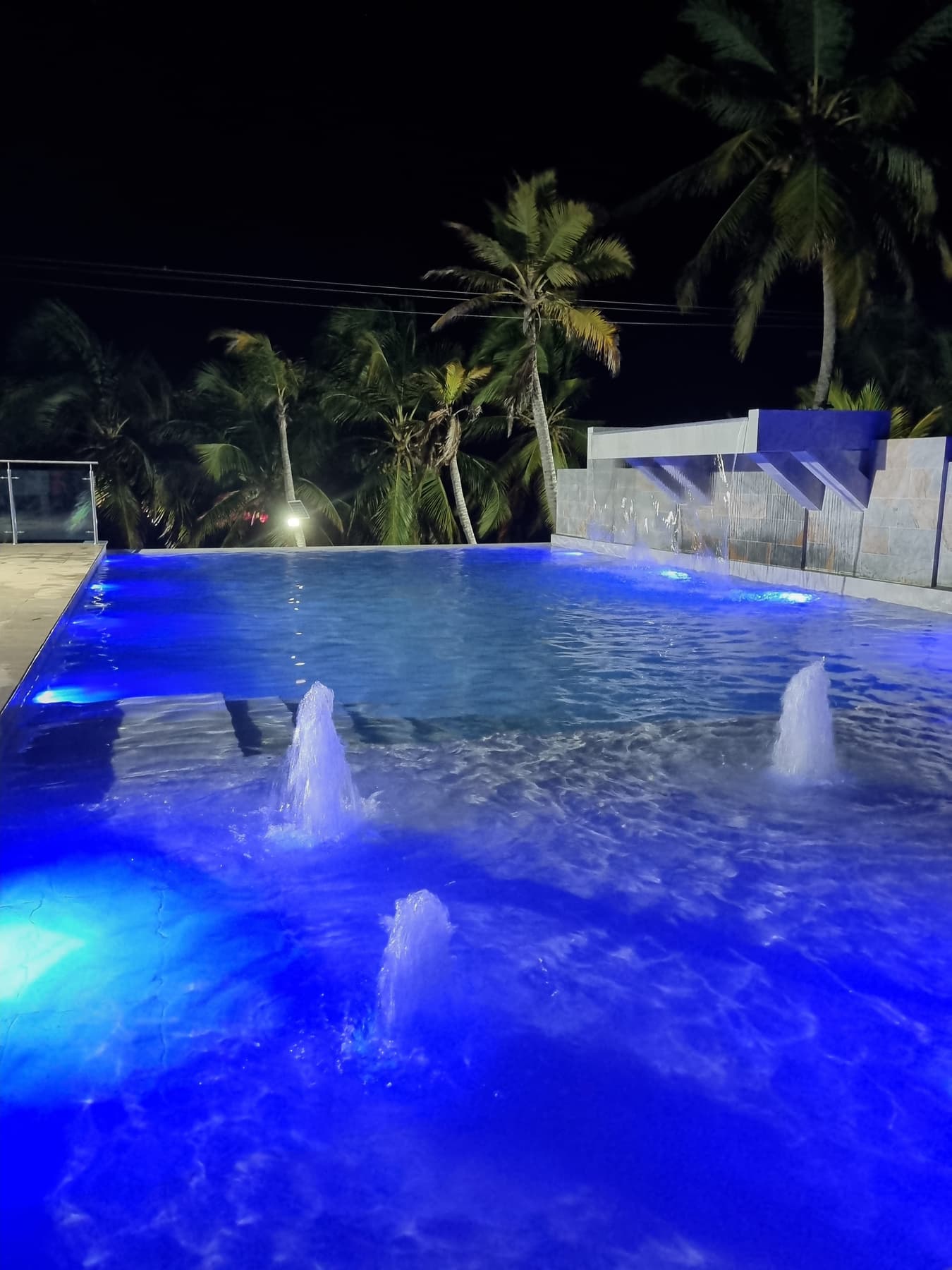 Piscina de Apartahotel Acapulco de noche, iluminada con luces azules entre palmeras