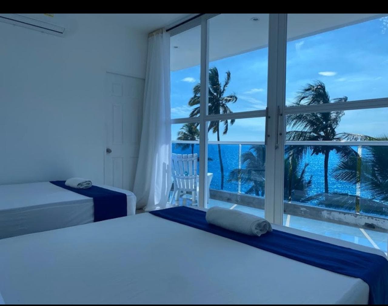 Habitación de Palma Linda con camas gemelas y vista al mar y palmeras desde el balcón